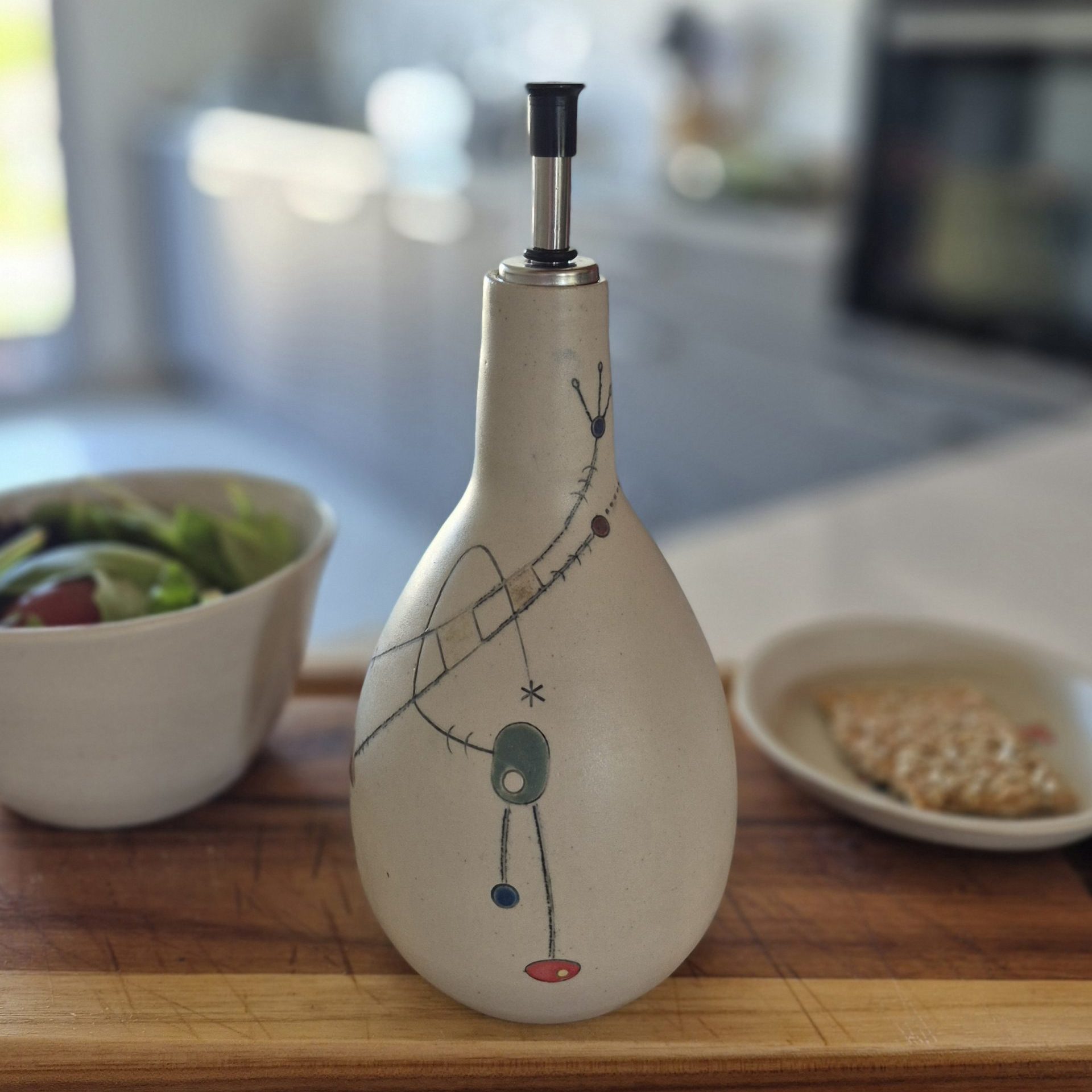 Huilier en céramique Géometrik avec décor graphique peint à la main, photographié sur une table en bois avec salade et assiette