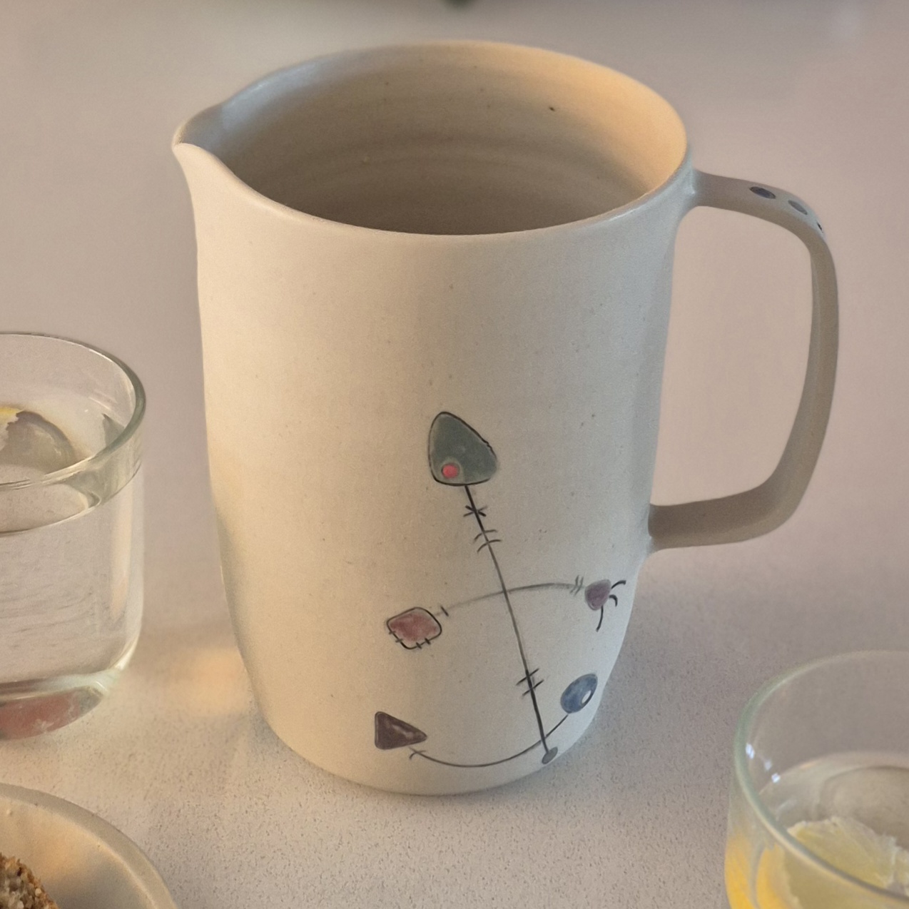 Vue rapprochée d’un pichet Géometrik en céramique artisanale avec bec verseur, anse et décor graphique peint à la main