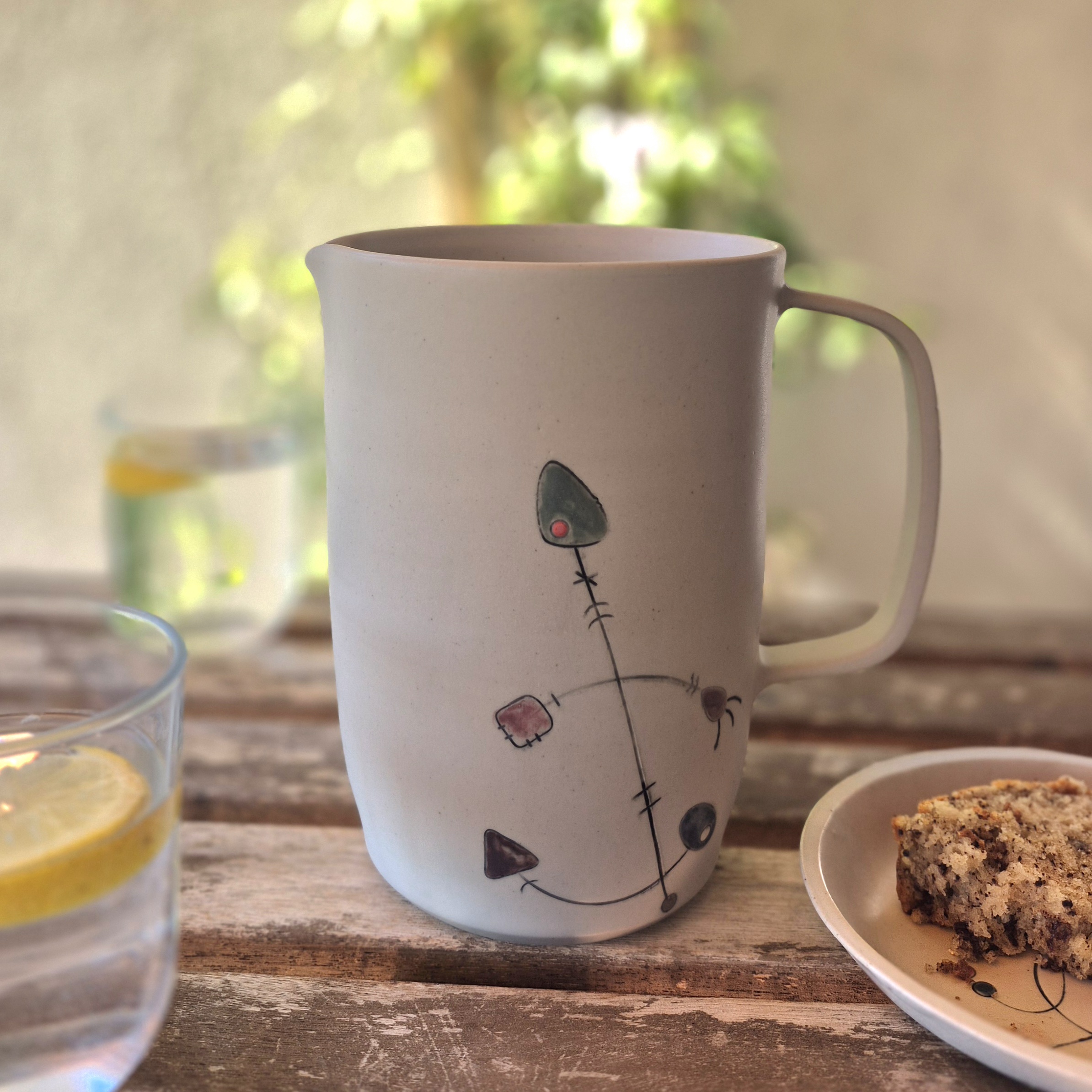 Pichet Géometrik en grès fait main avec décor graphique peint aux engobes, posé sur une table en bois avec citronnade et gâteau