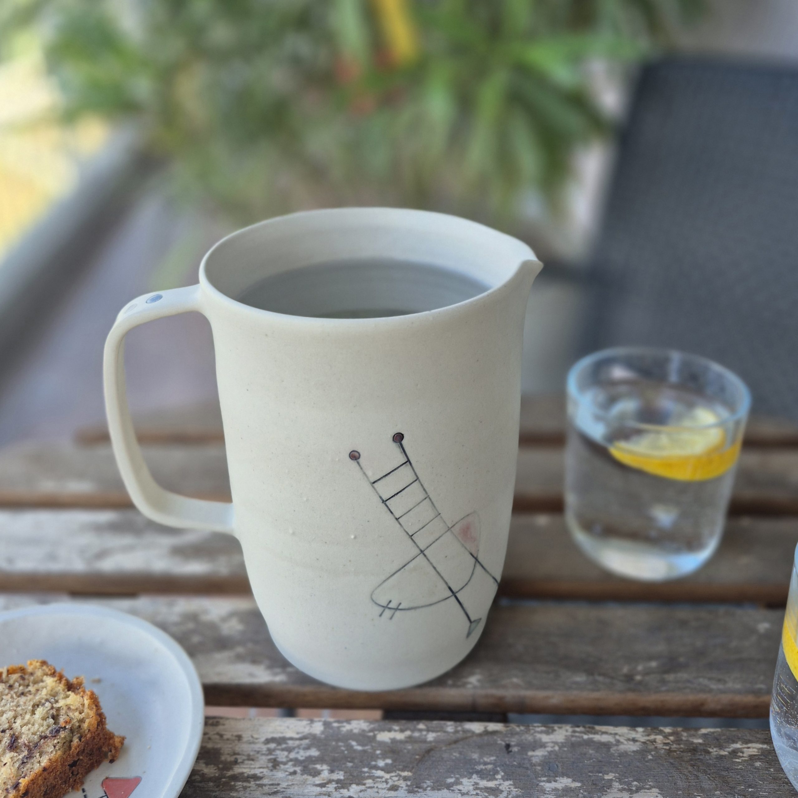 Pichet Géometrik en céramique artisanale avec décor graphique peint à la main, posé sur une table en bois avec verre d’eau citronnée