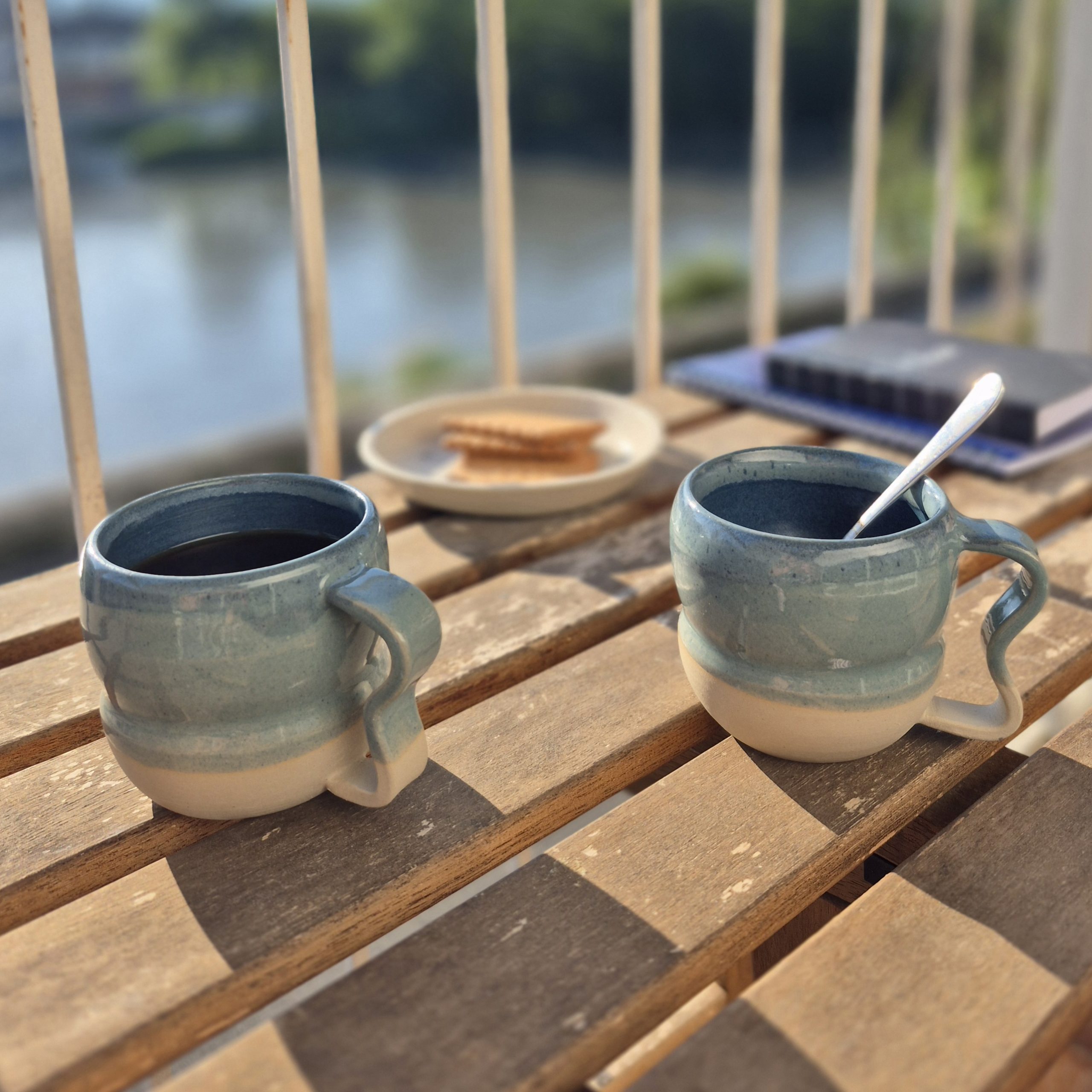 Deux tasses à café artisanales bleu turquoise sur une terrasse au bord de l’eau – Atelier Kaolin Grenoble